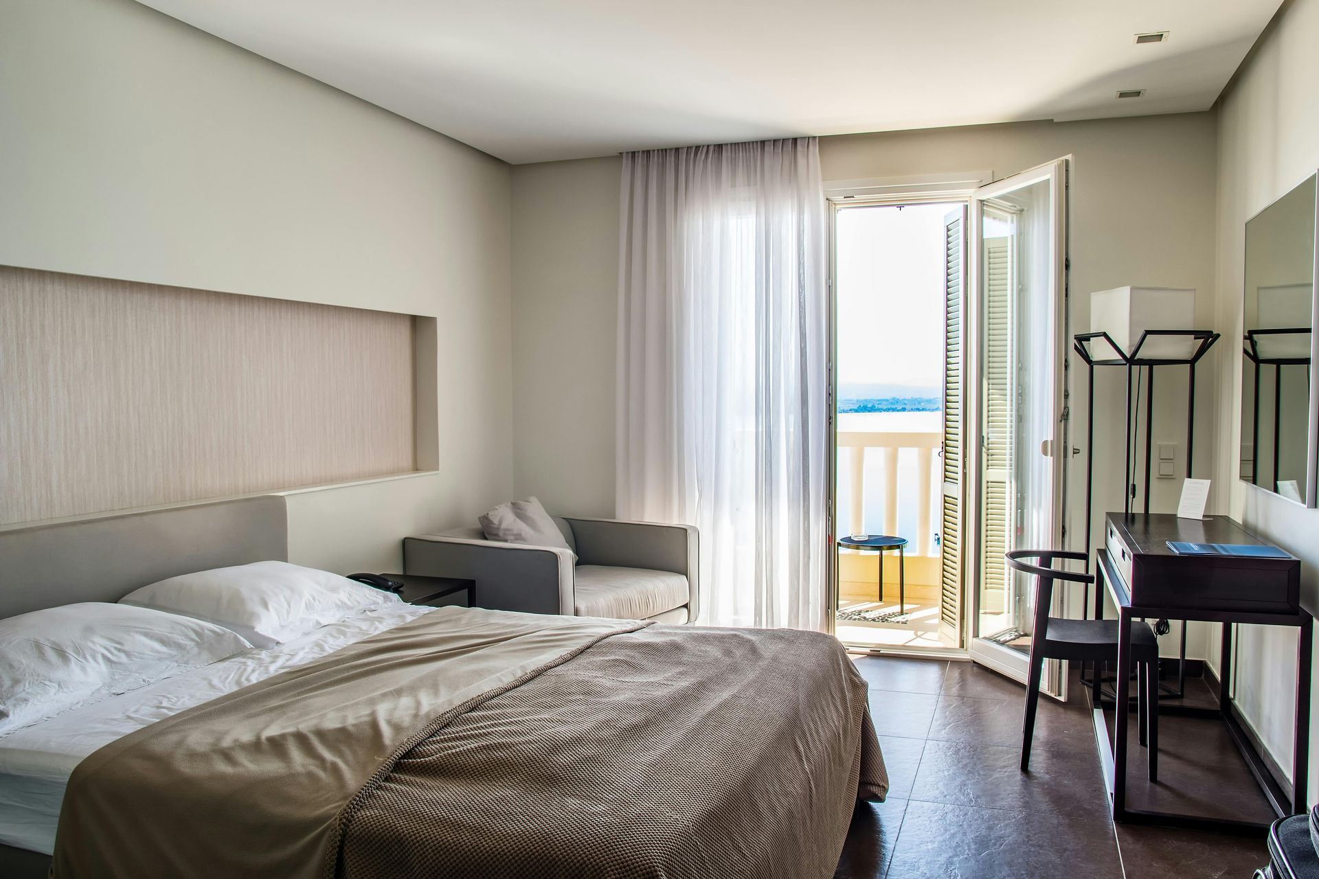 A hotel room with a large bed , desk , chair and balcony.