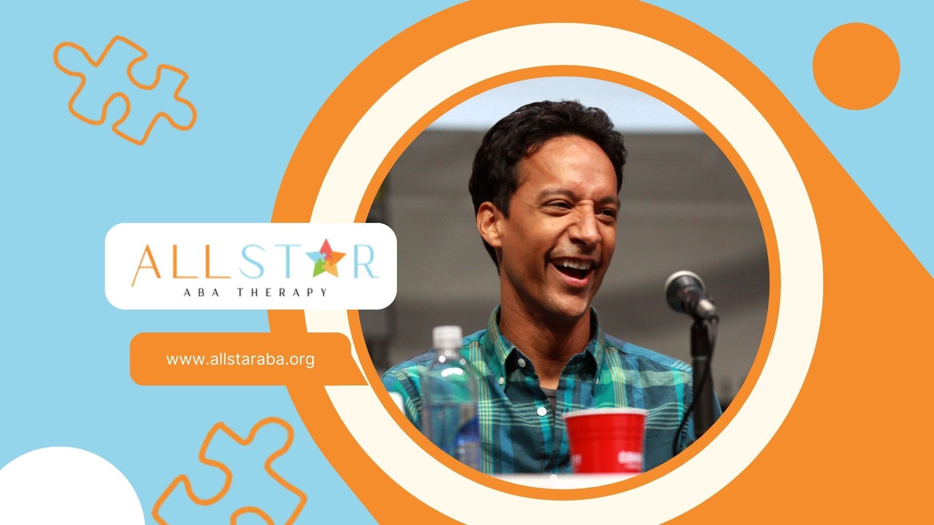 Actor Danny Pudi is laughing while standing in front of a microphone.