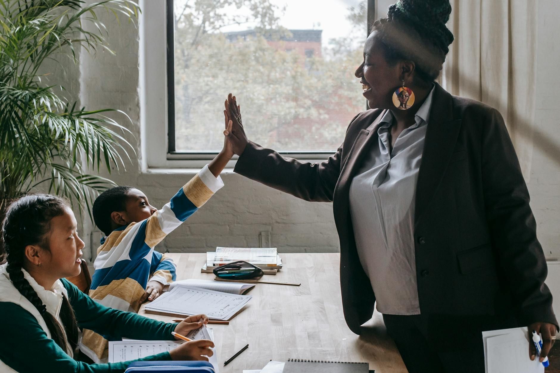 A woman giving a high five to a child in a classroom.