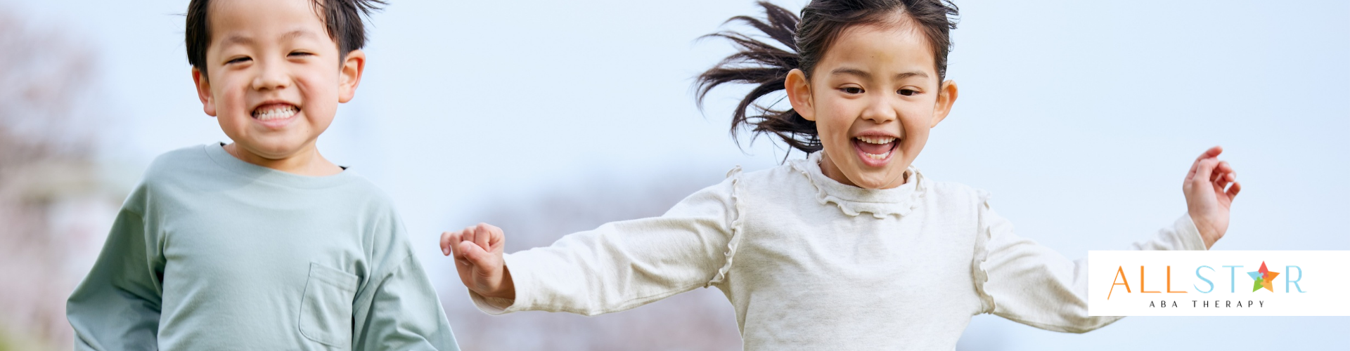 Two children, smiling, running outside. One wears blue, the other white.