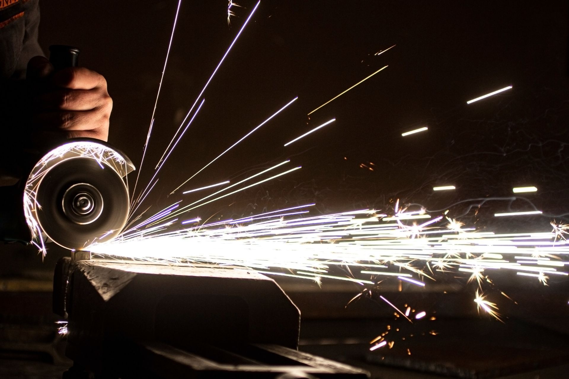 Close up of a worker cutting metal with an angle grinder, creating bright sparks.