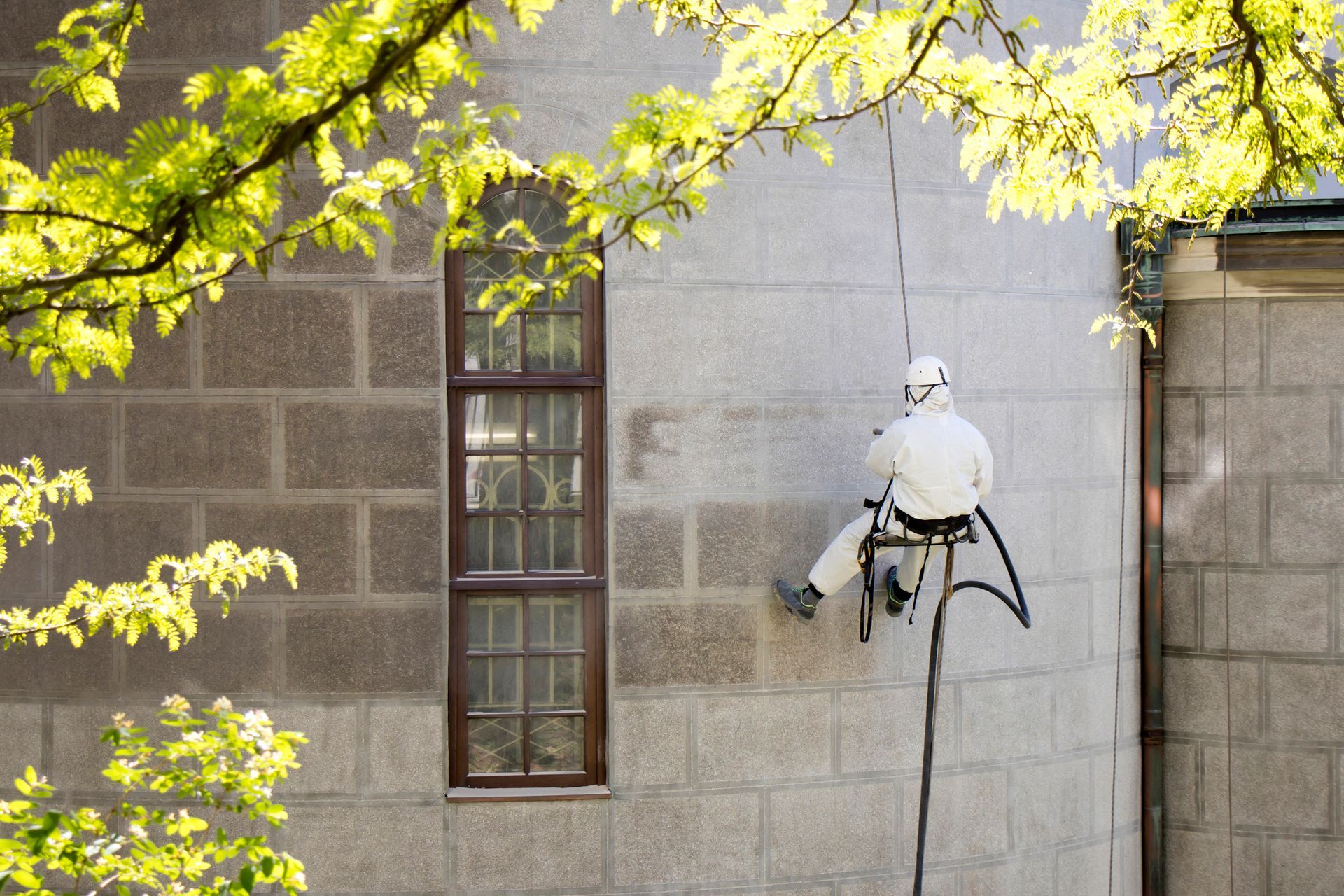 A worker wearing protective gear cleans the exterior of a church with abrasive blasting equipment.