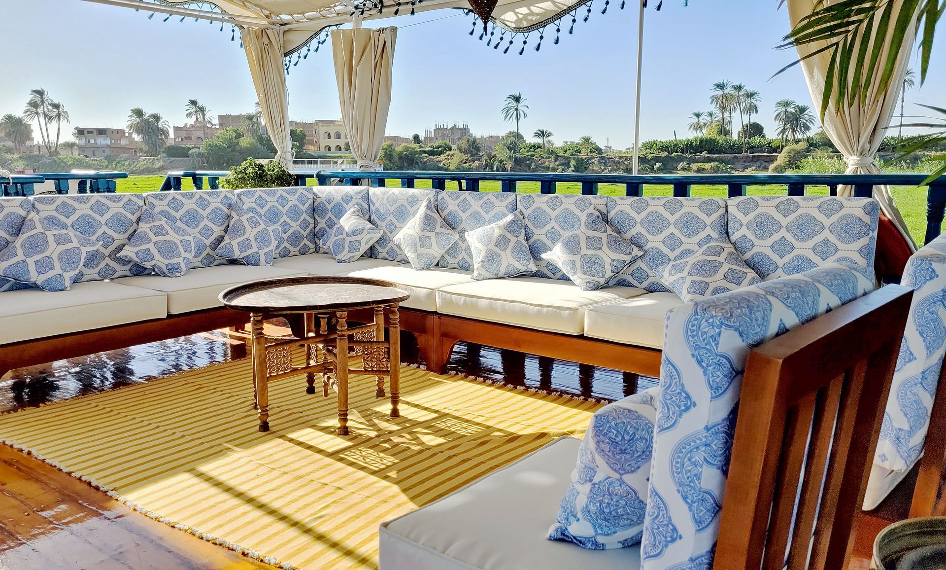 A photo of a cozy seating area on the deck of a traditional Egyptian sailing boat, the Dahabiya Kingfisher, which offers private cruises along the Nile river between Luxor and Aswan.
