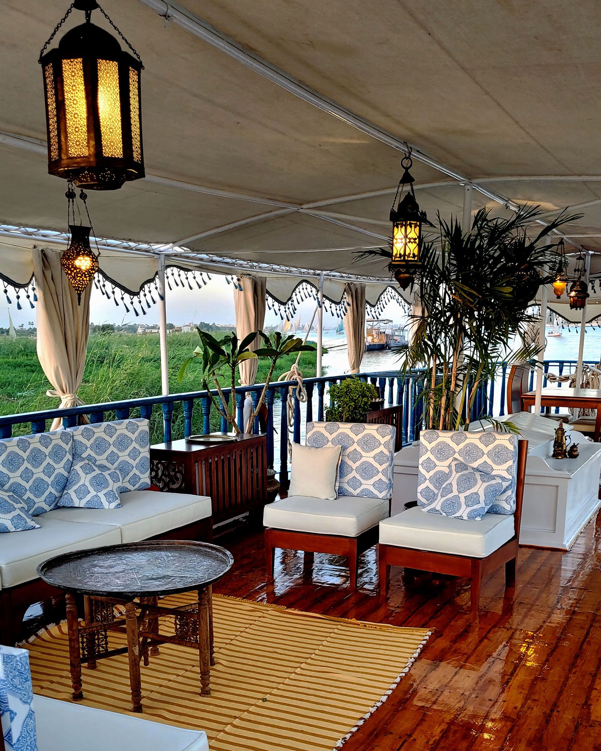 A photo of a cozy seating area on the deck of a traditional Egyptian sailing boat, the Dahabiya Kingfisher, which offers private cruises along the Nile river between Luxor and Aswan.