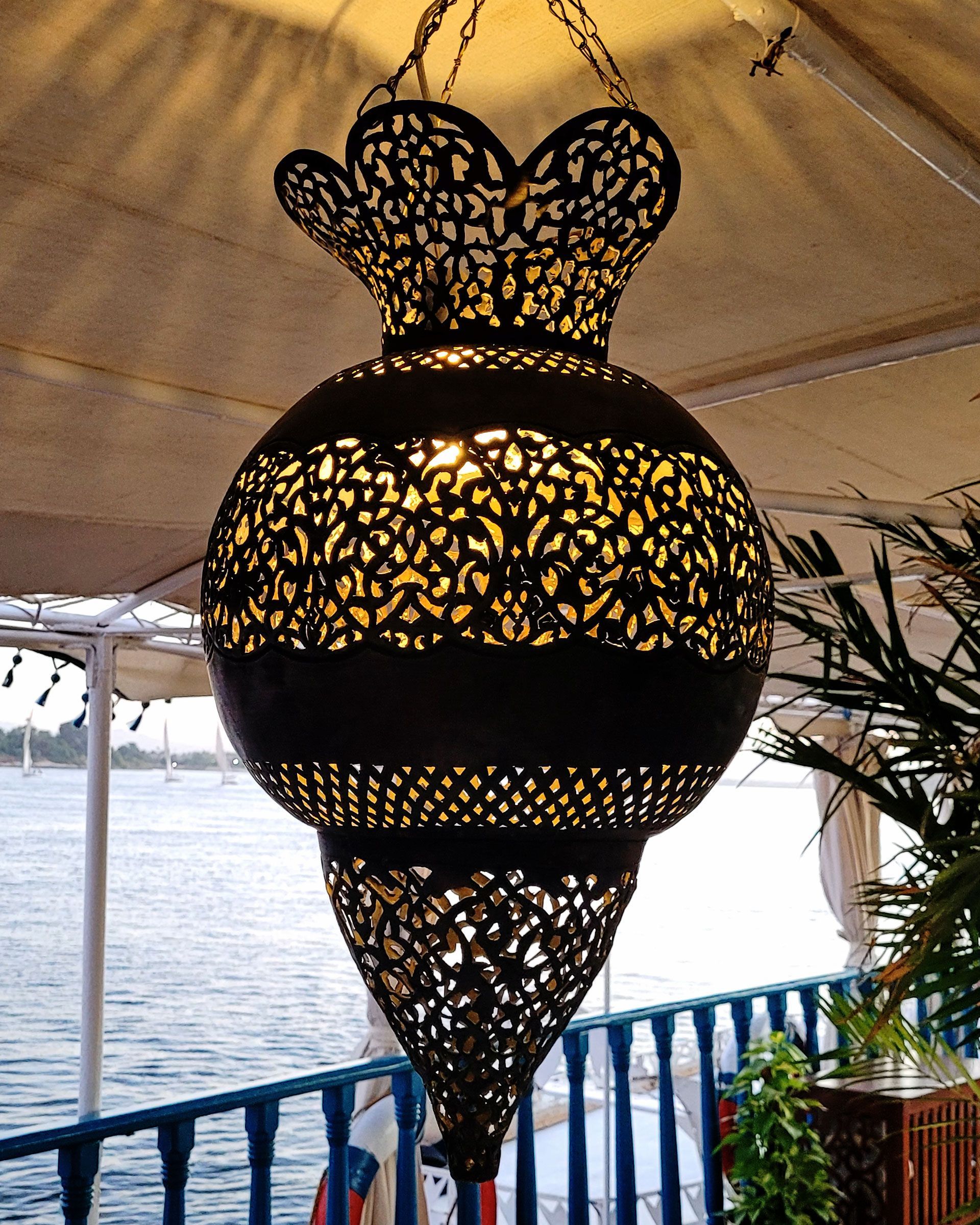 An antique copper lamp on a historic boat sailing the Nile. The boat is the Dahabiya Kingfisher, which was built in 1899 and offers private cruises between Luxor and Aswan in Egypt.