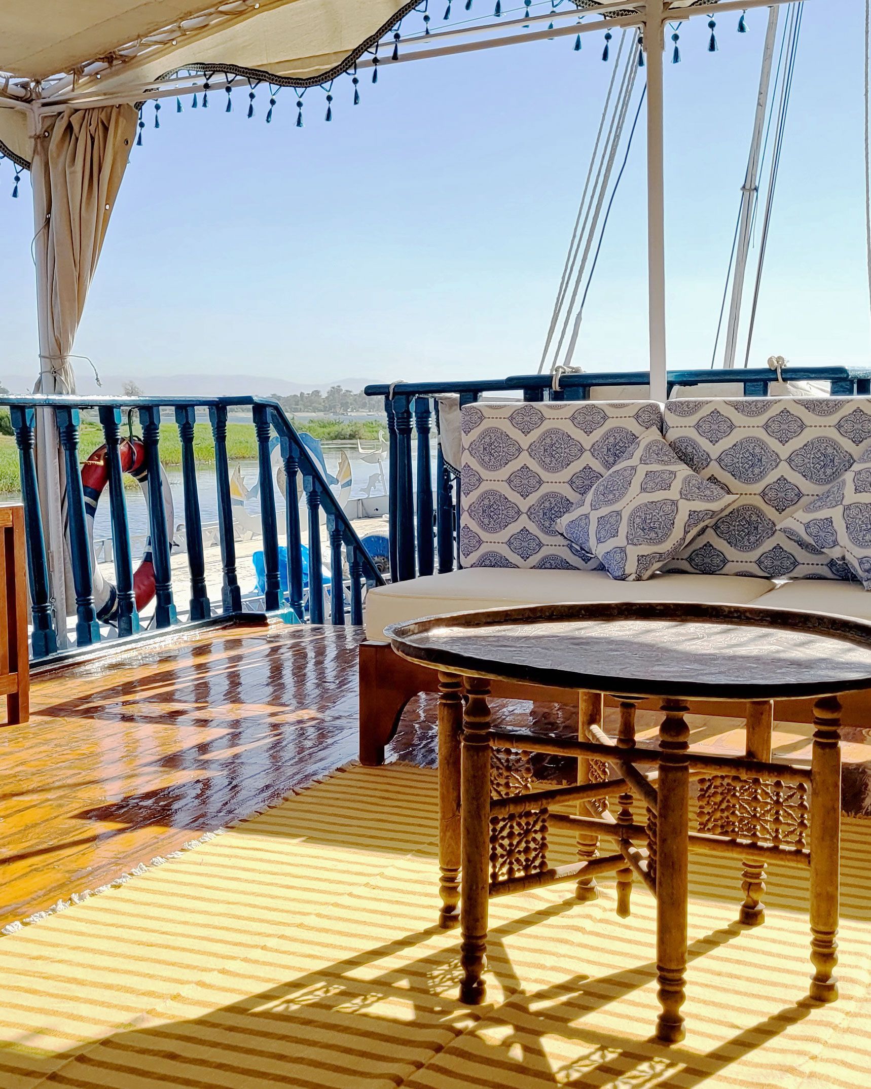 A photo of a cozy seating area on the deck of a traditional Egyptian sailing boat, the Dahabiya Kingfisher, which offers private cruises along the Nile river between Luxor and Aswan.