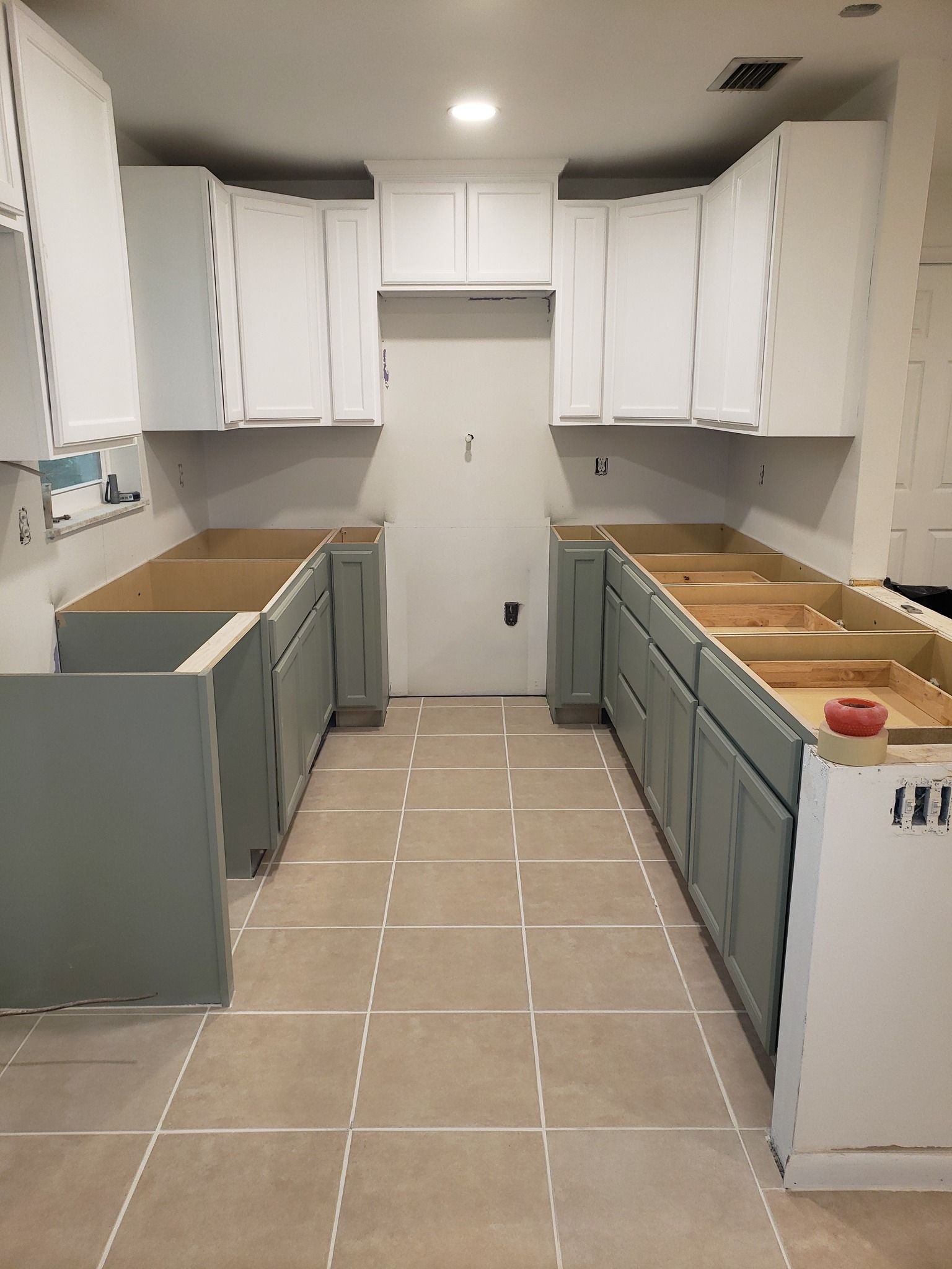 Kitchen with gray and white cabinets being installed, with tan tile flooring.