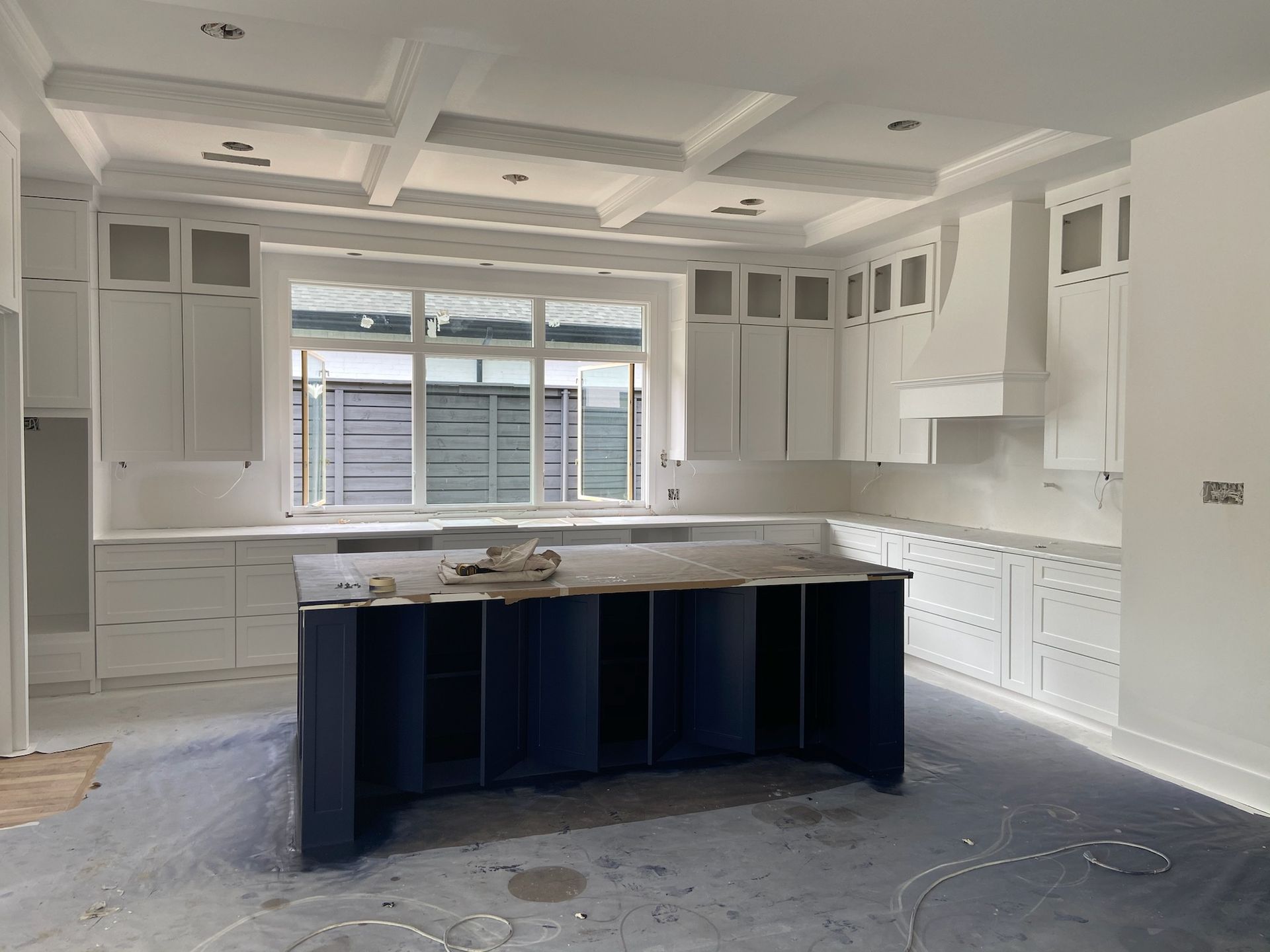 Kitchen with white cabinets, blue island, and coffered ceiling.