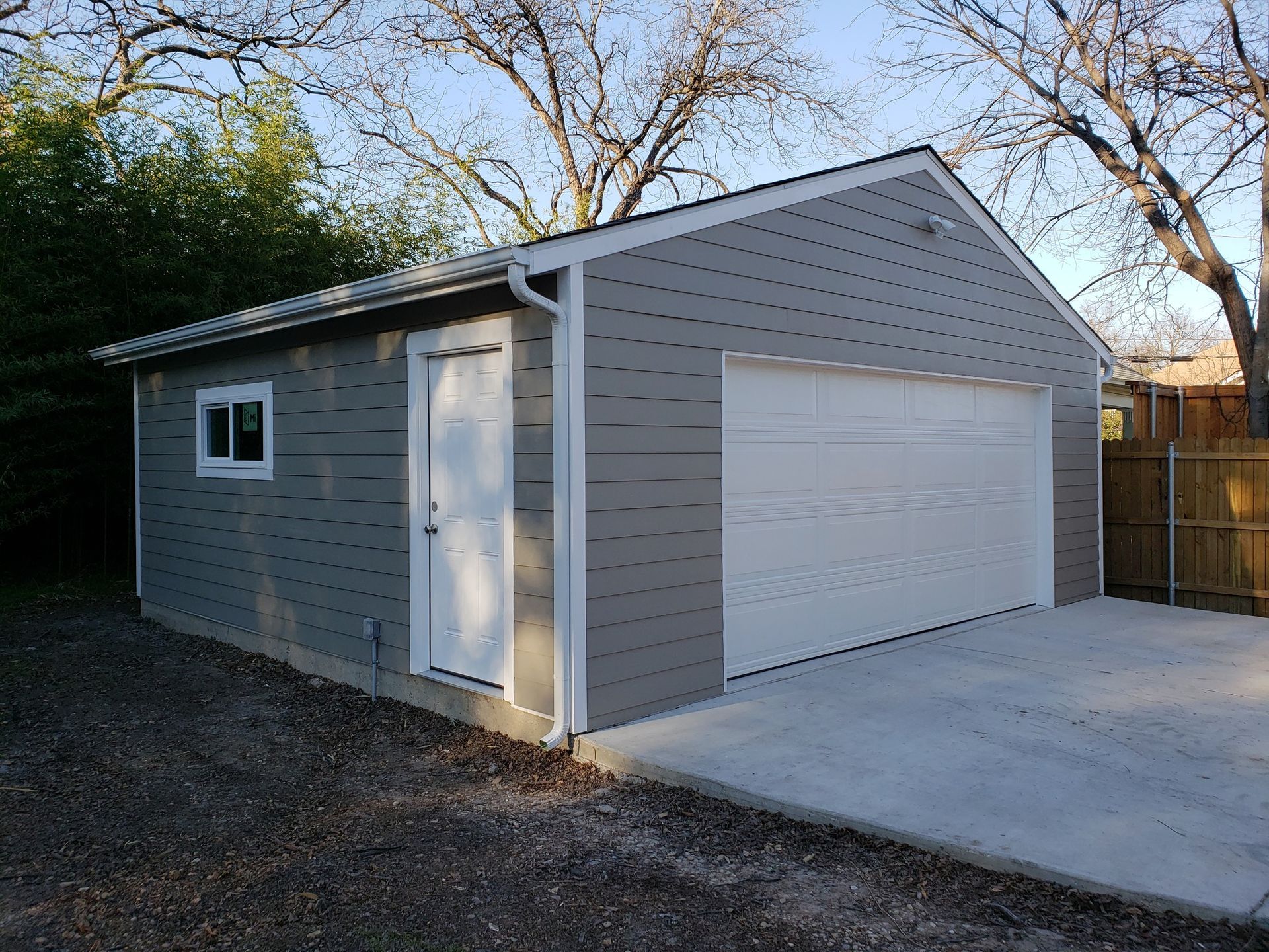 Gray garage with white door and garage door, concrete driveway, and a small window.