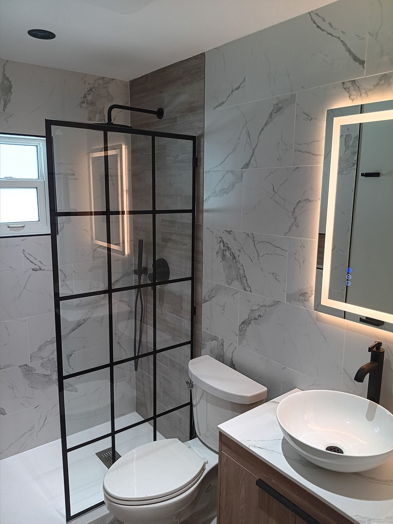 Modern bathroom with a glass shower, marble tile walls, and a vessel sink.