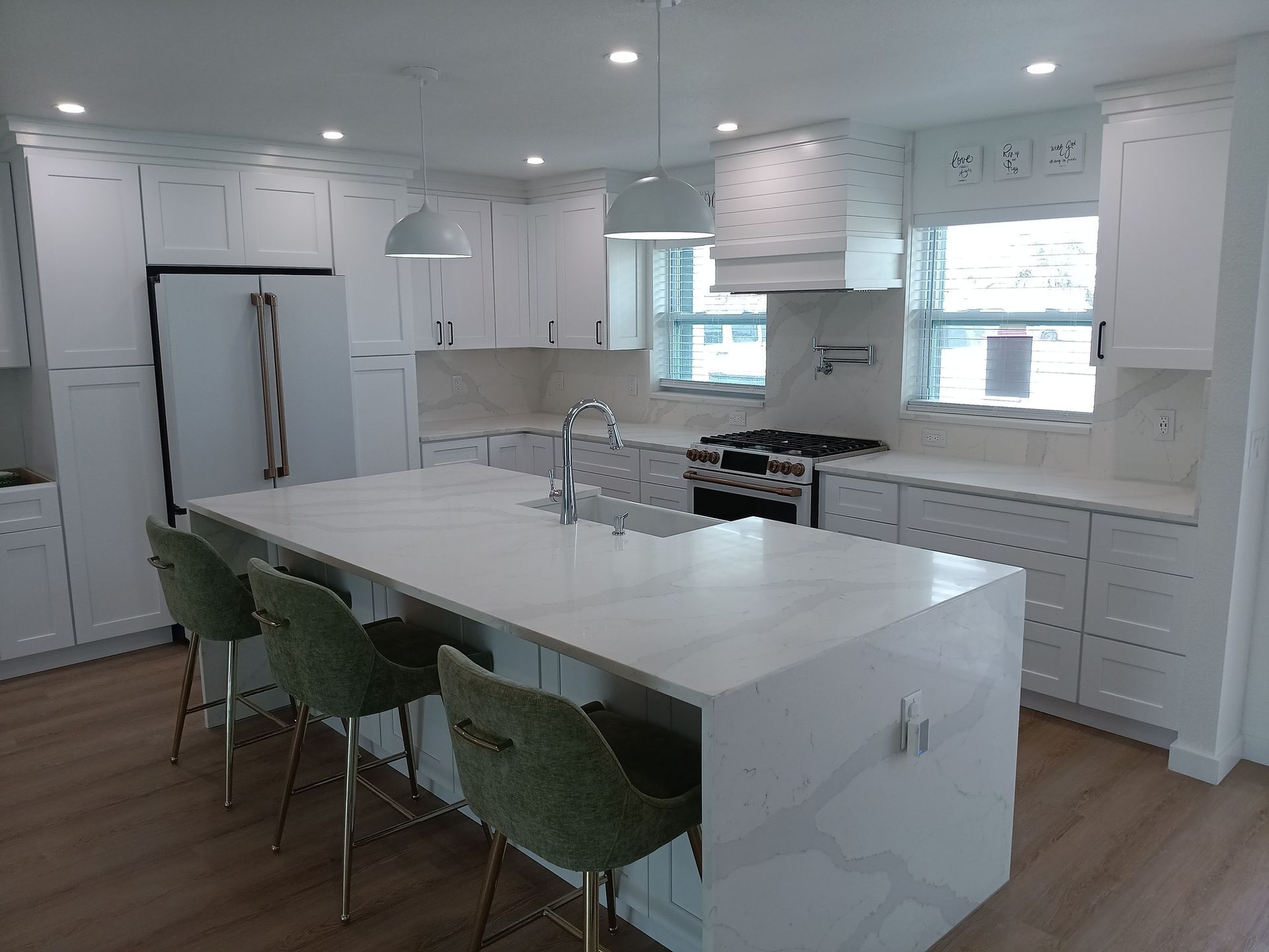 Modern white kitchen with island, seating, and stainless steel appliances.