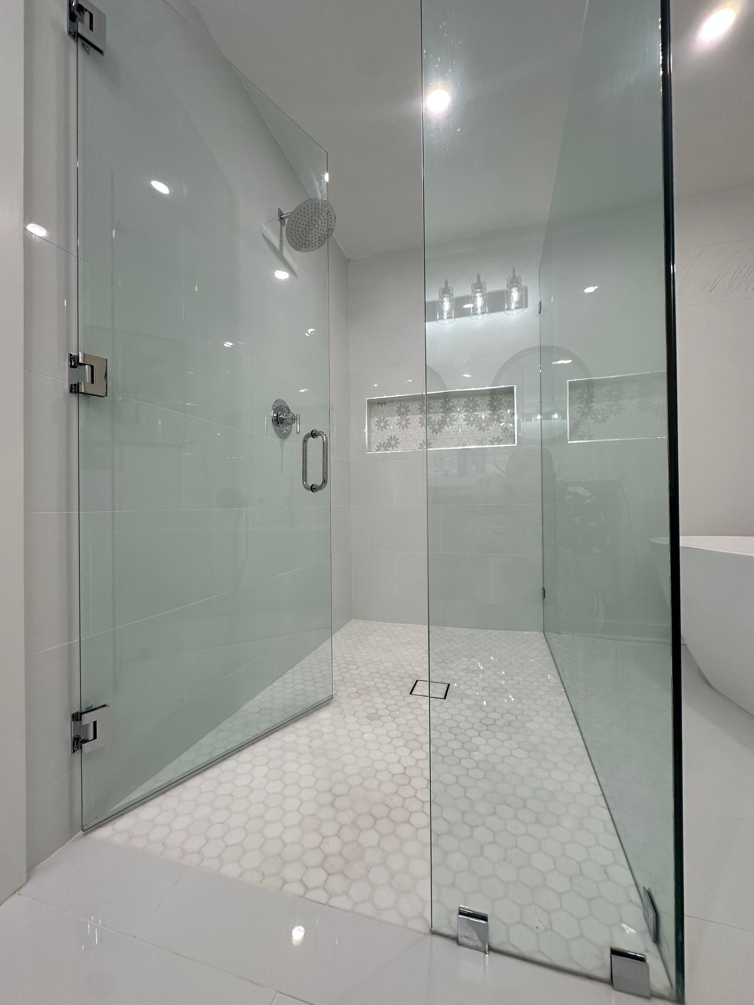 Glass shower enclosure with white tiled walls and floor. Chrome fixtures.