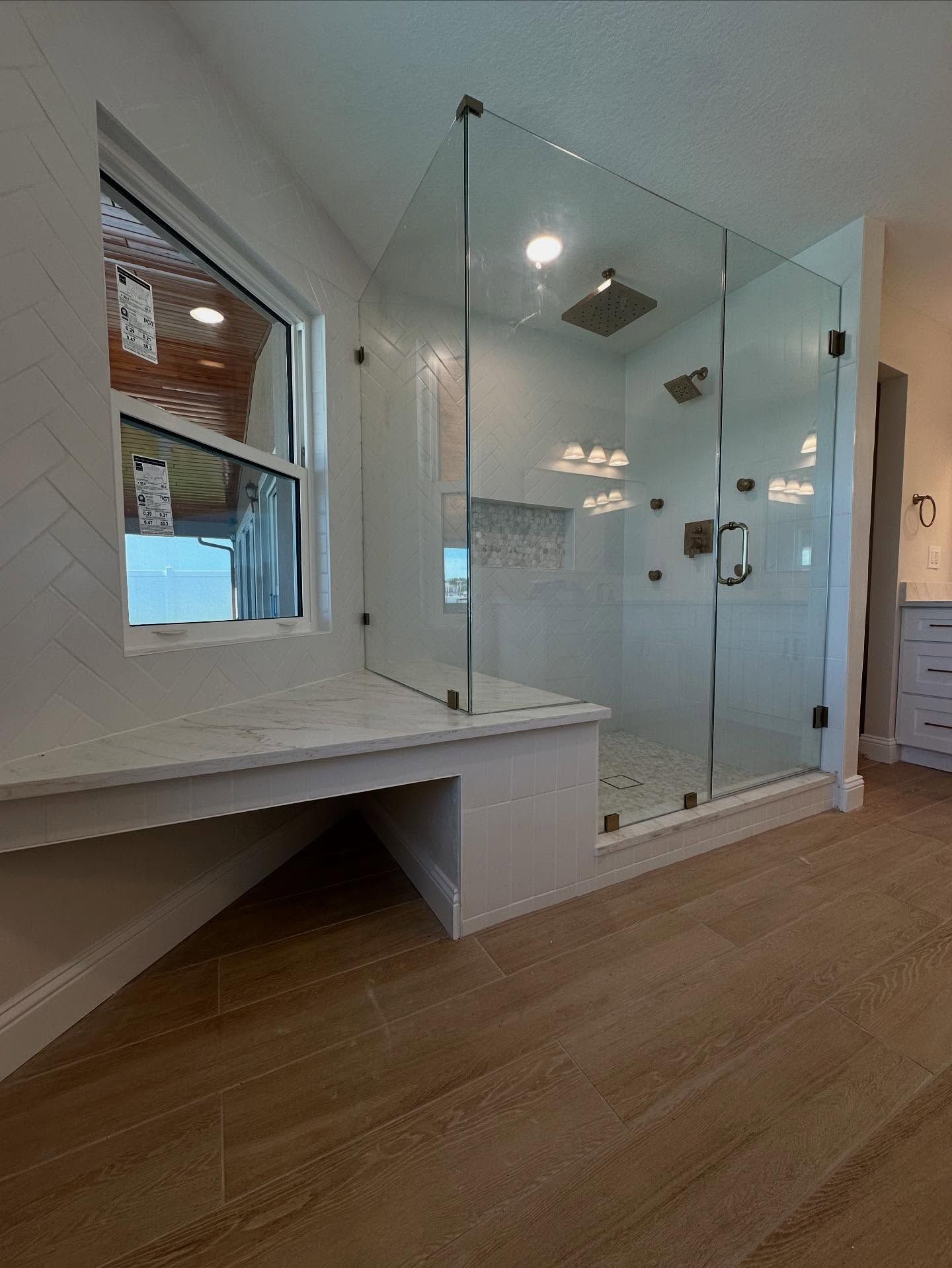 Modern bathroom with glass shower, built-in bench, white tile, and wood-look flooring.
