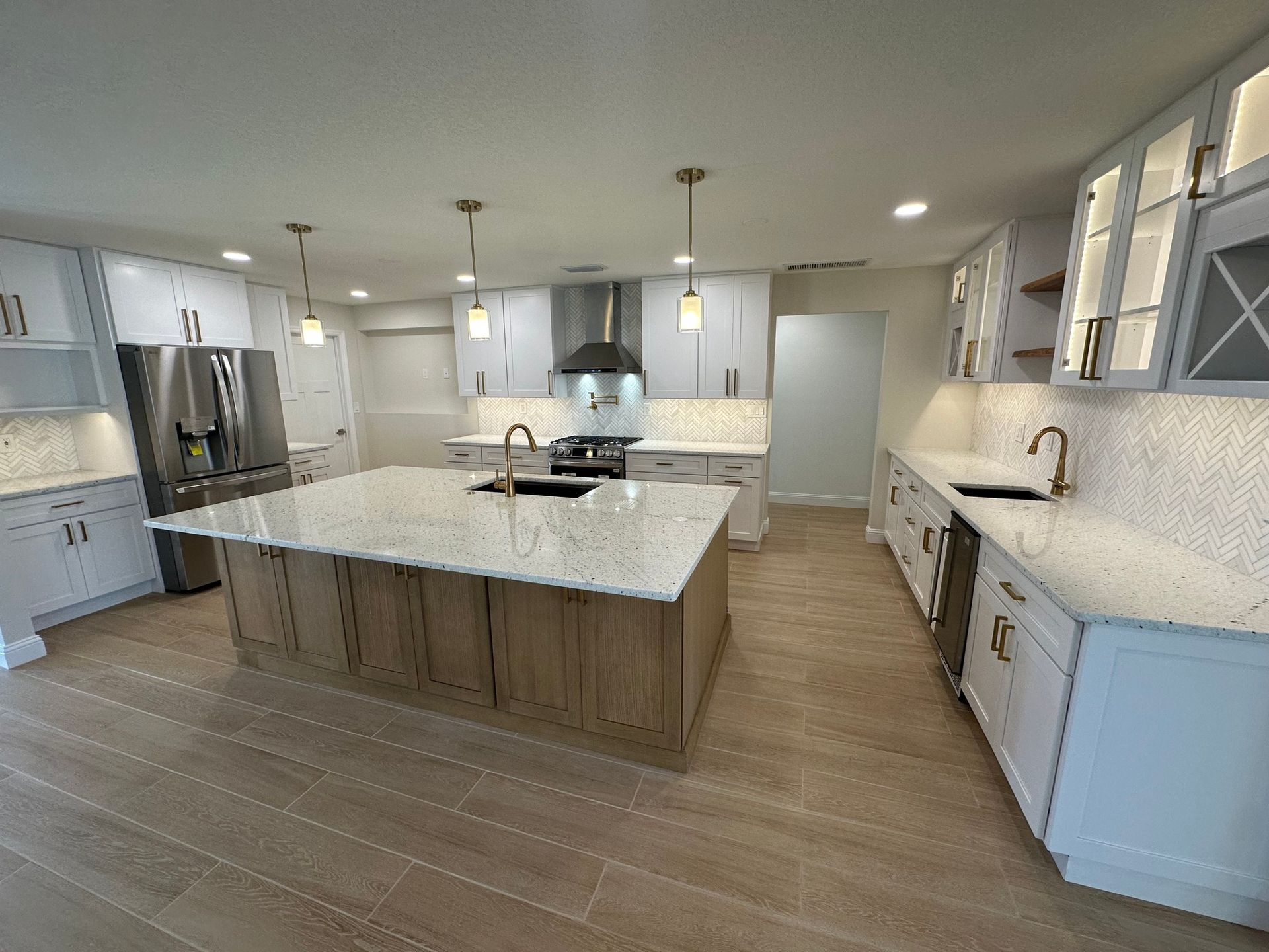 Modern white kitchen with large island and light wood flooring.