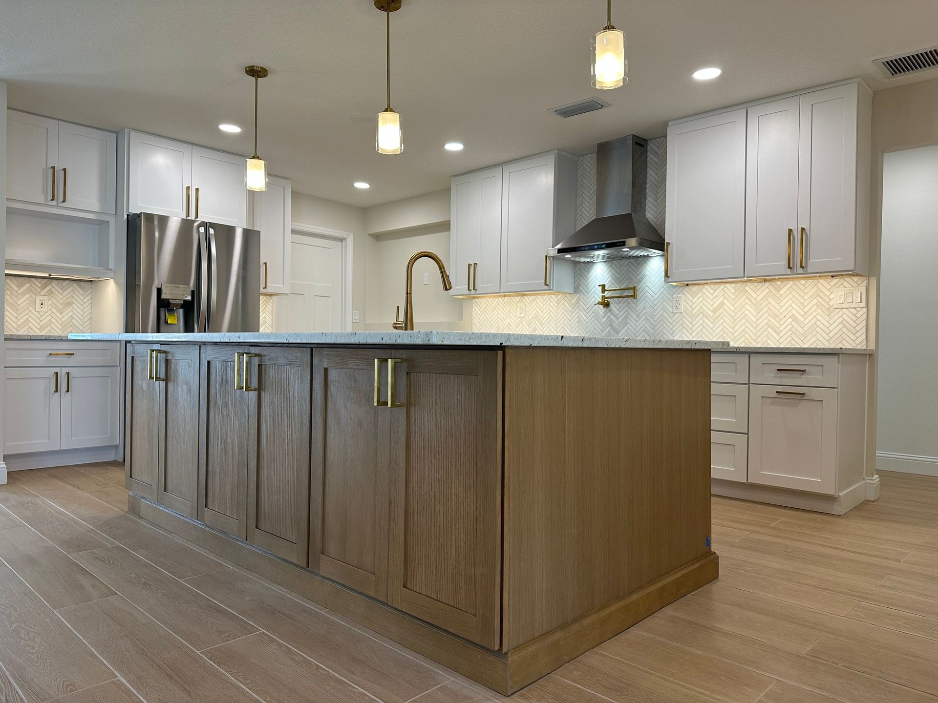 Modern kitchen with a wooden island, white cabinets, stainless steel appliances, and gold hardware.