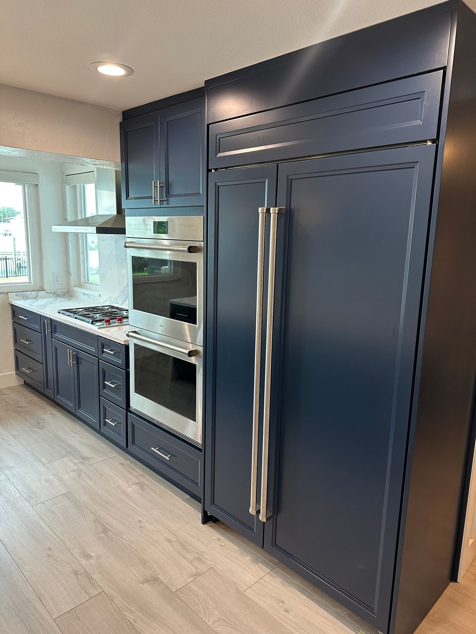 Navy blue kitchen cabinets and refrigerator with stainless steel handles.
