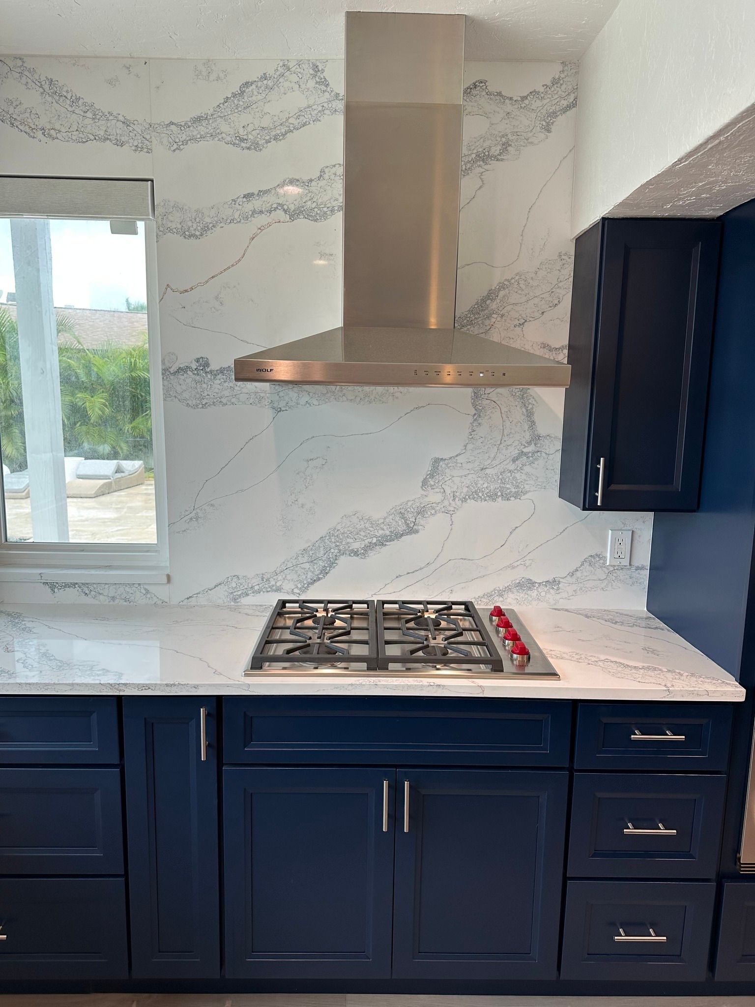 Kitchen with blue cabinets, gas stovetop, stainless steel range hood, and white countertops and backsplash.