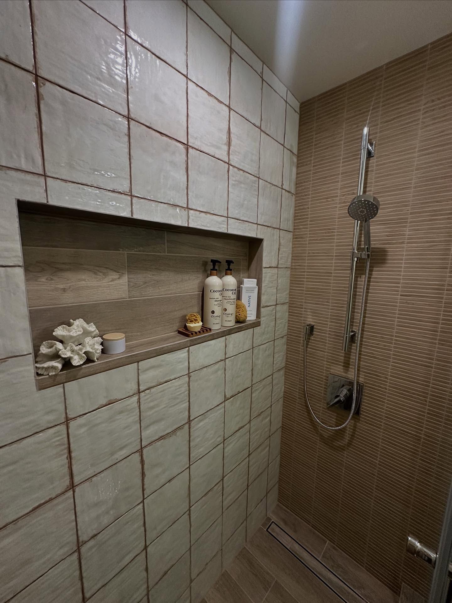 Shower stall with beige and brown tiles, built-in shelf with toiletries.