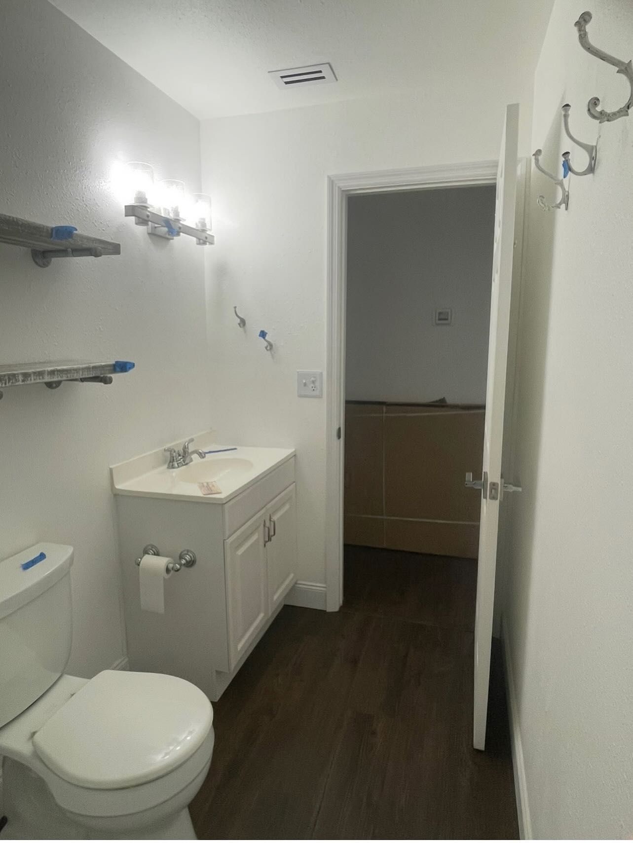 Bathroom with white sink and toilet, open doorway, brown floor, and coat rack.