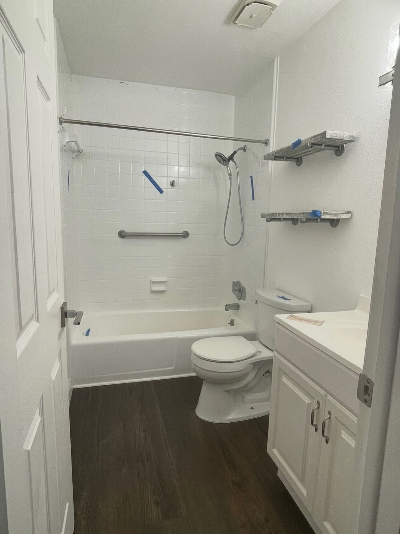 Bathroom with white fixtures, dark wood floor, and handrails.