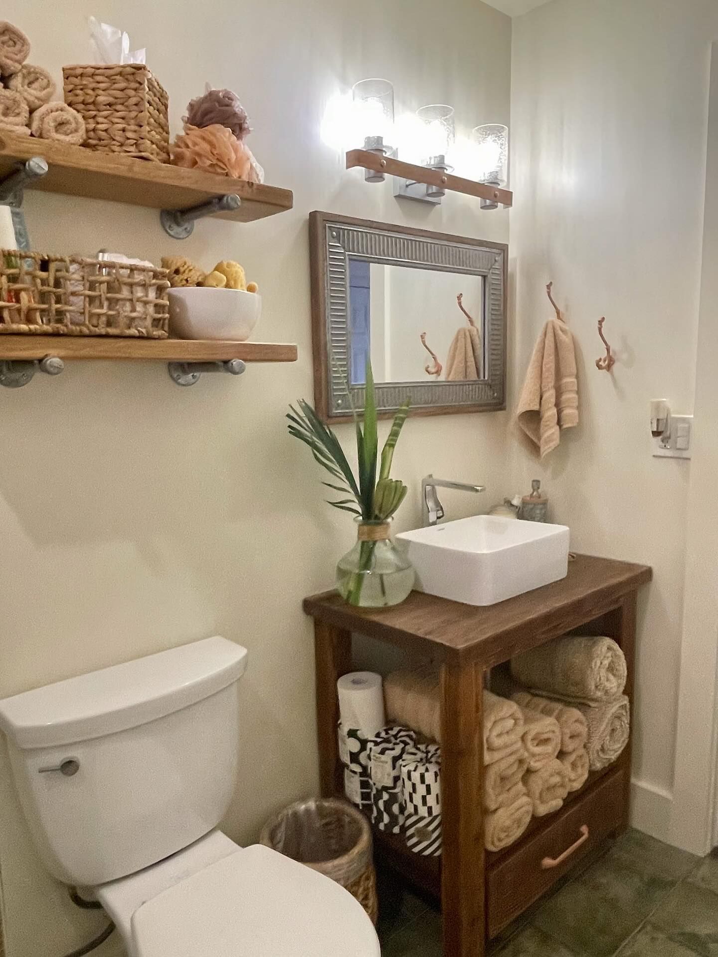 Bathroom with wood shelves and vanity, white sink and toilet, and neutral-colored towels.