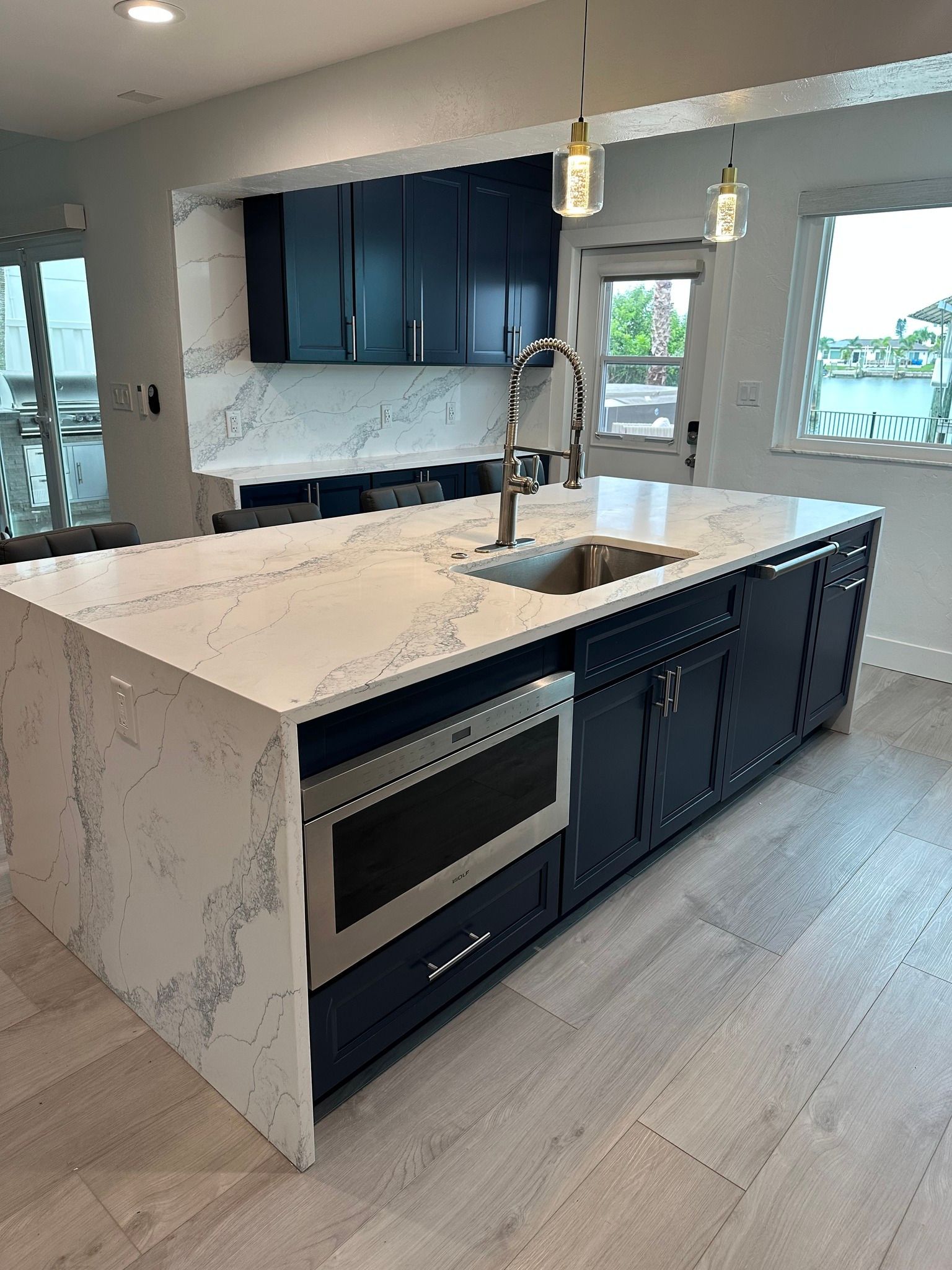 Modern kitchen island with dark blue cabinets, white countertop, stainless steel microwave and sink.