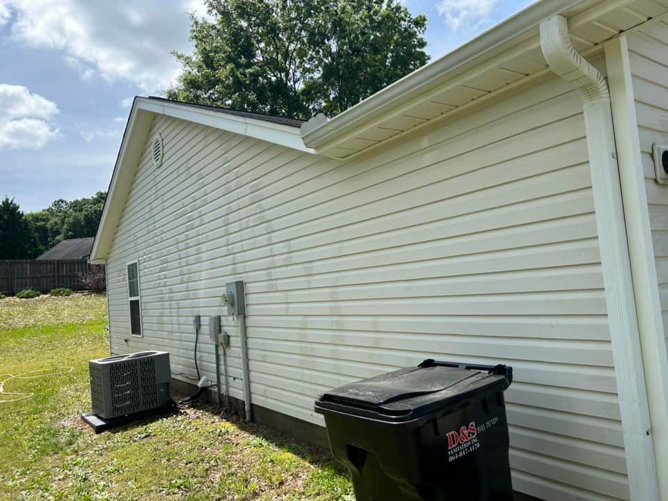 A white house with a black trash can and air conditioner on the side of it.