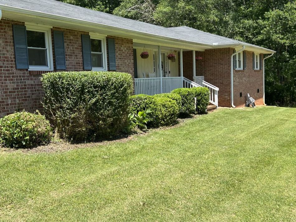 A brick house with blue shutters and a large lawn in front of it.