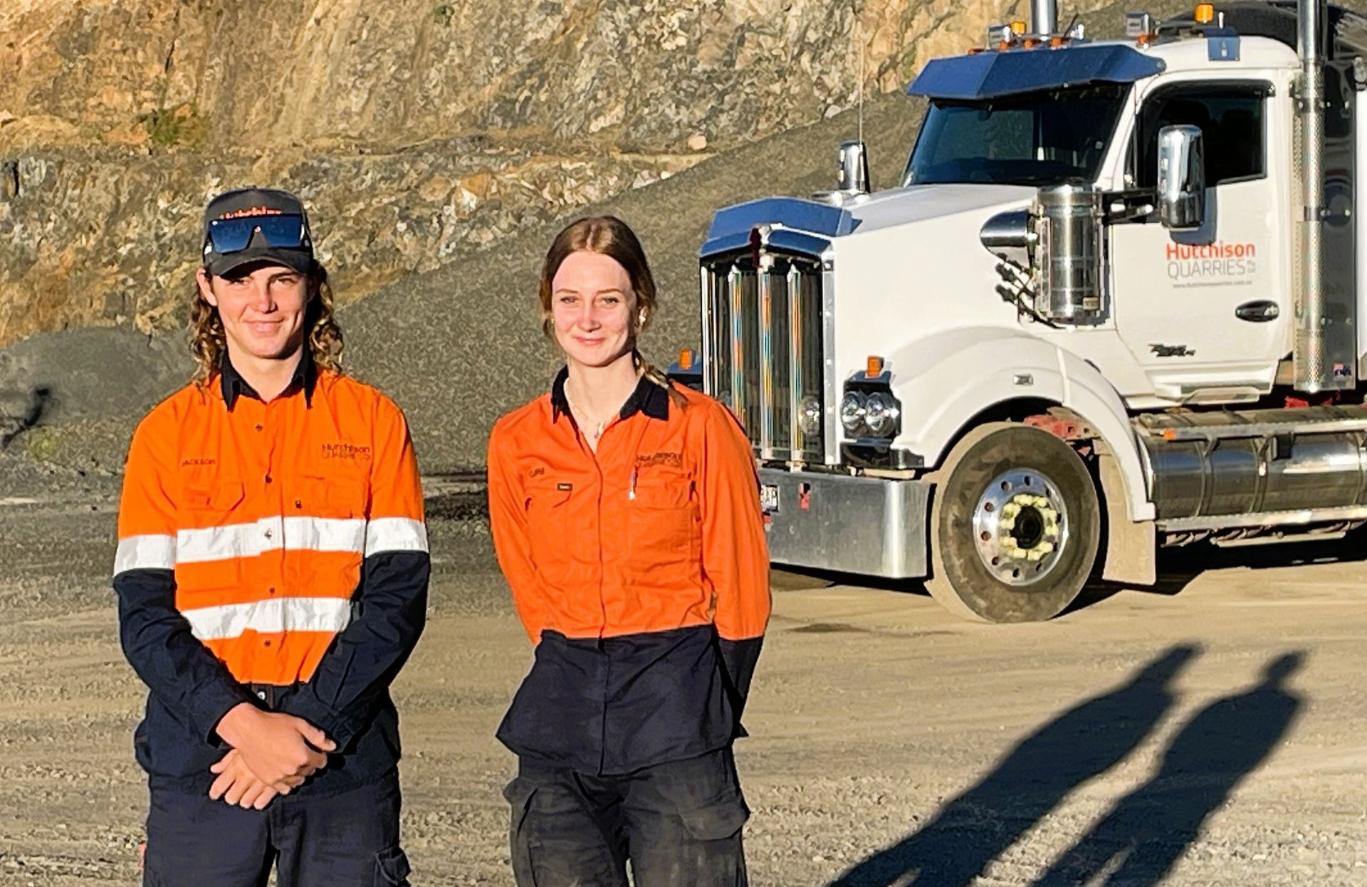 Jackson and Claire in orange high-vis stand near a large white Hutchison Quarries truck in a quarry.