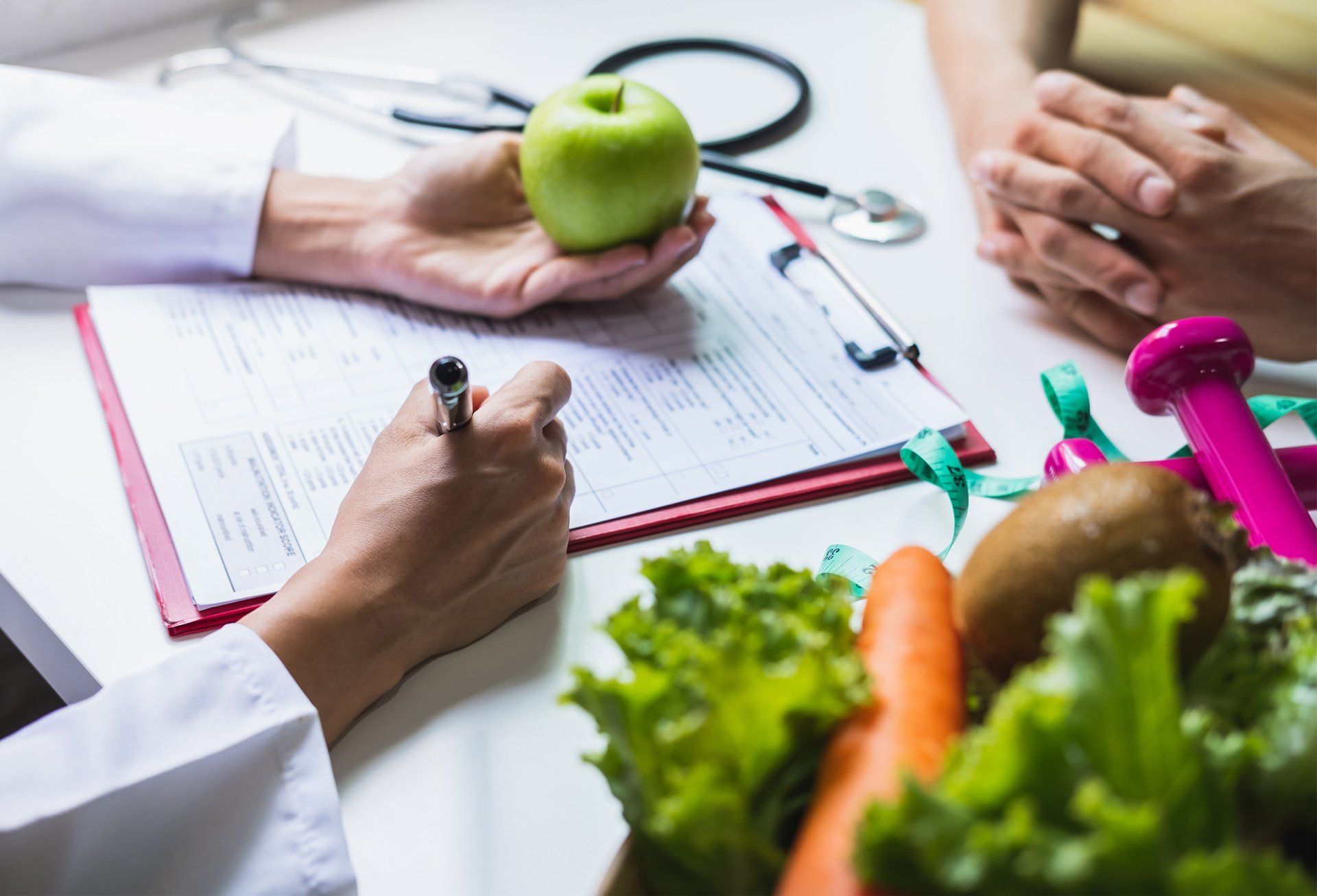 A woman is holding an apple while a doctor writes on a clipboard.