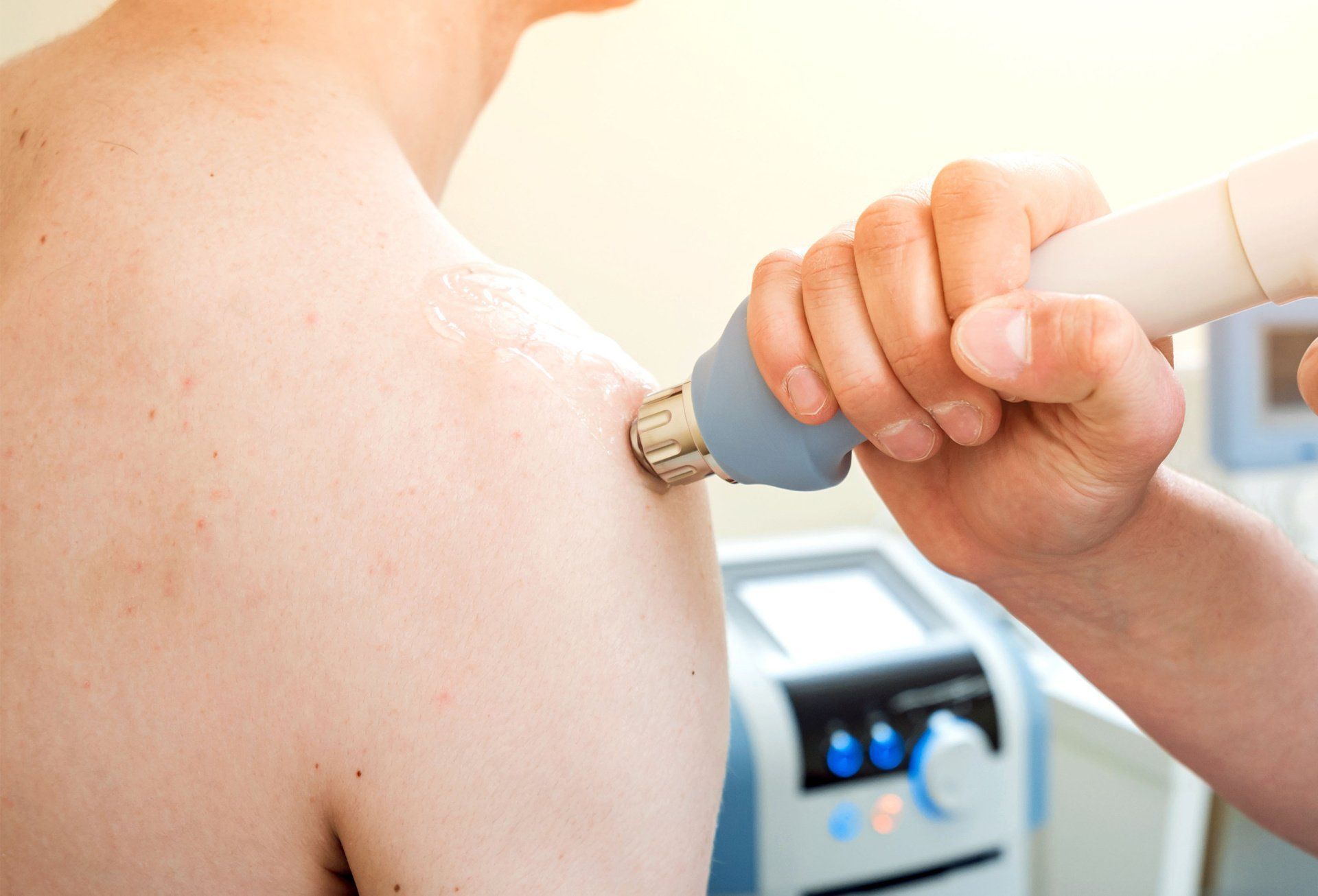 A person is using a machine on a man's shoulder.
