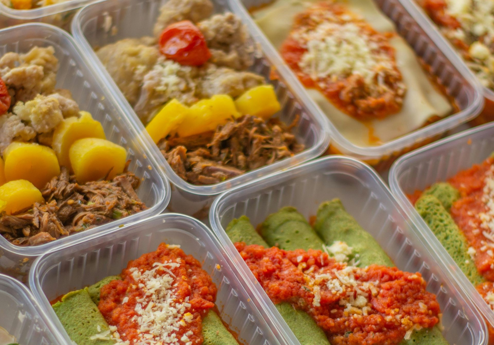 Meal prep containers filled with various dishes: pasta, crepes, and sides.