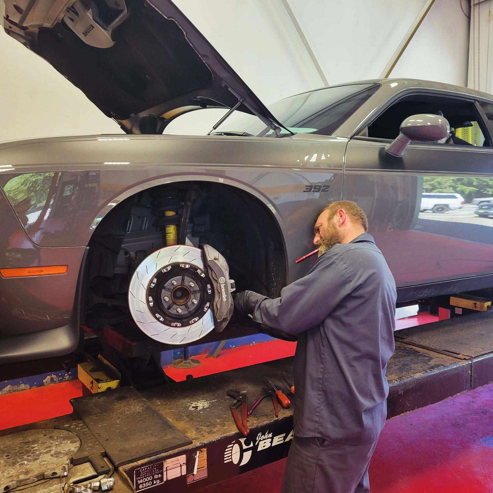 A man is working on a dodge challenger with the hood open | Auto Check Automotive Ltd.