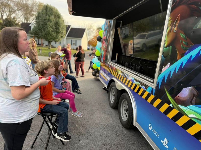 A group of children are sitting in front of a video game truck.