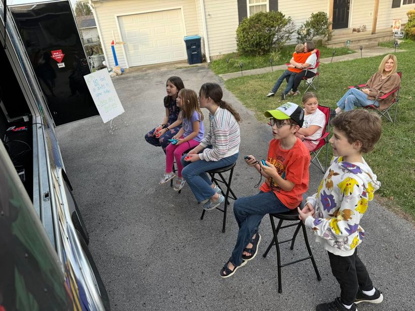 A group of children are sitting on stools in front of a food truck.