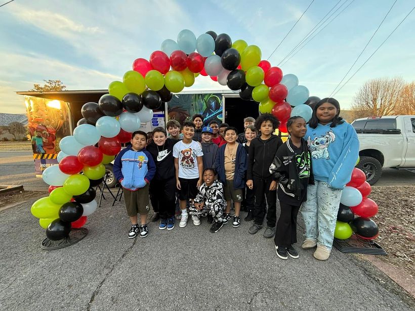 A group of children are posing for a picture in front of a balloon arch.