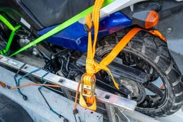 A motorcycle wheel and blue frame secured to a trailer with orange ratchet straps and a green tie-down strap.