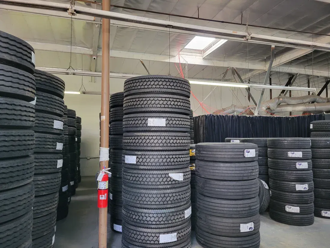 Stacks of tires in a warehouse, lit by skylights. Some tires have price tags.