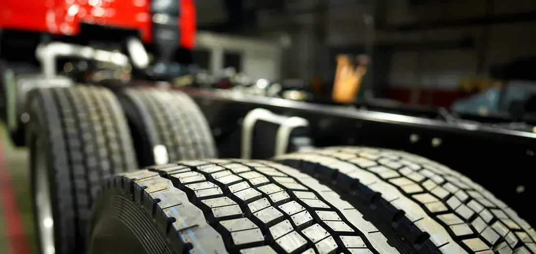 Close-up view of truck tires. Red truck cab is in background; black chassis visible. Tires have a textured tread pattern.