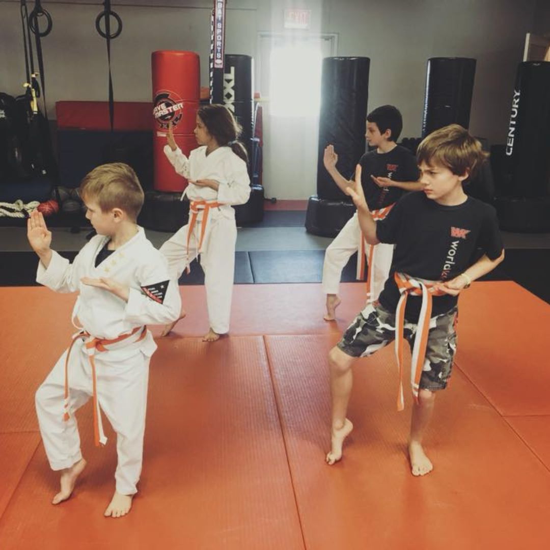 A young girl in a karate uniform is sitting on the floor.
