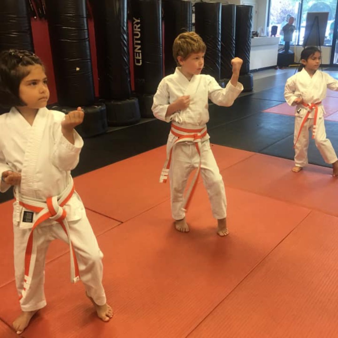 A young girl in a karate uniform is sitting on the floor.