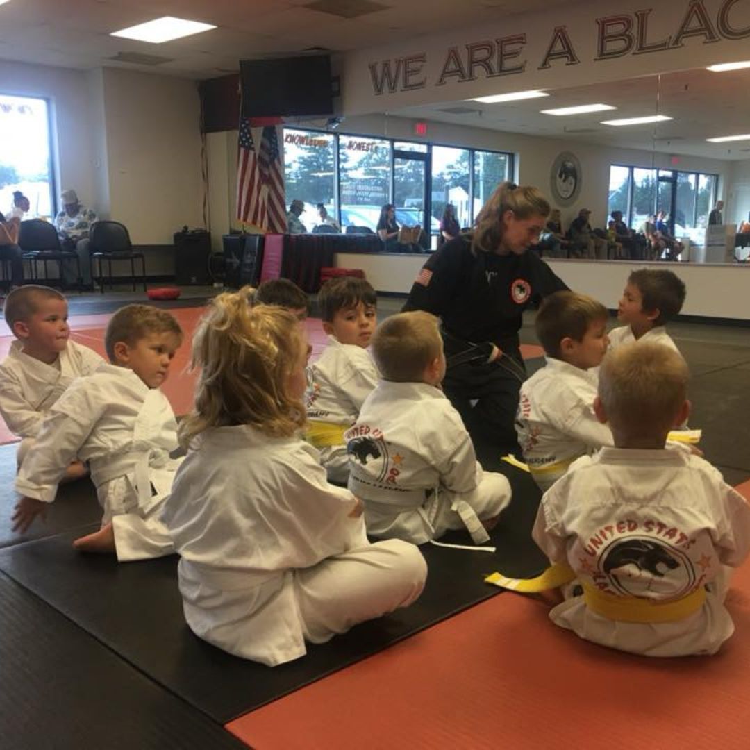 A group of children are practicing karate with a teacher in a gym.