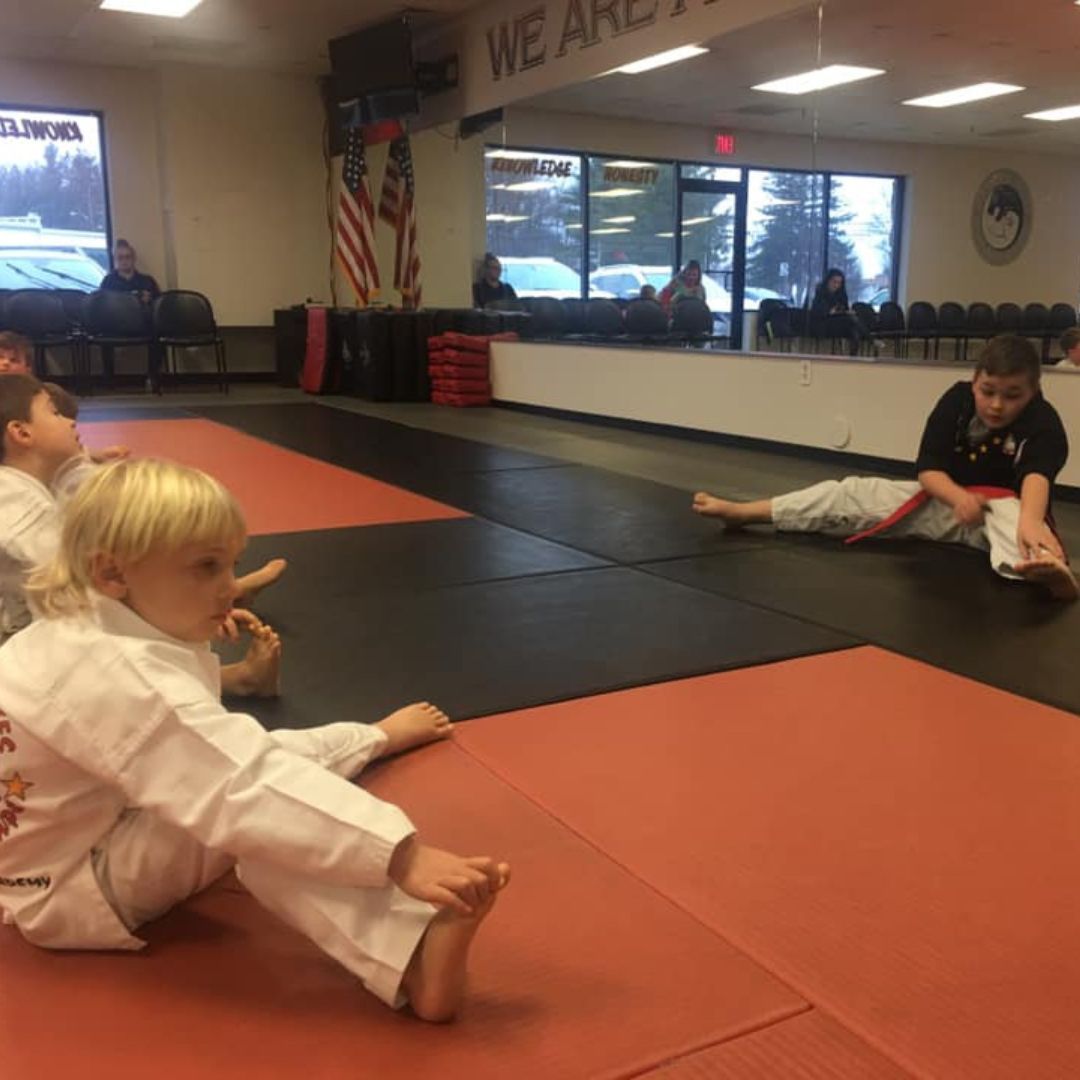 A group of children are practicing karate with a teacher in a gym.