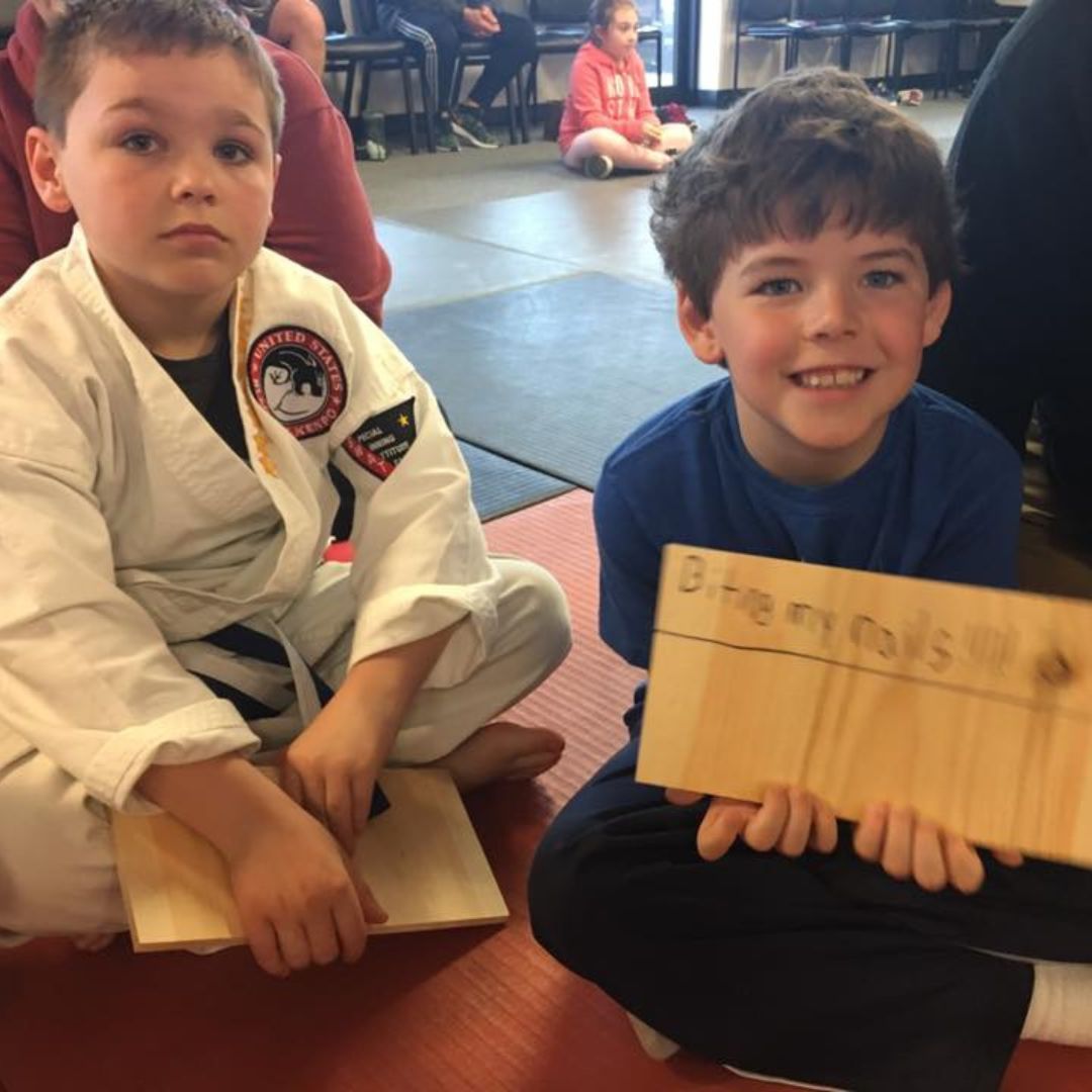 A man is kneeling down next to a young boy in a taekwondo class.