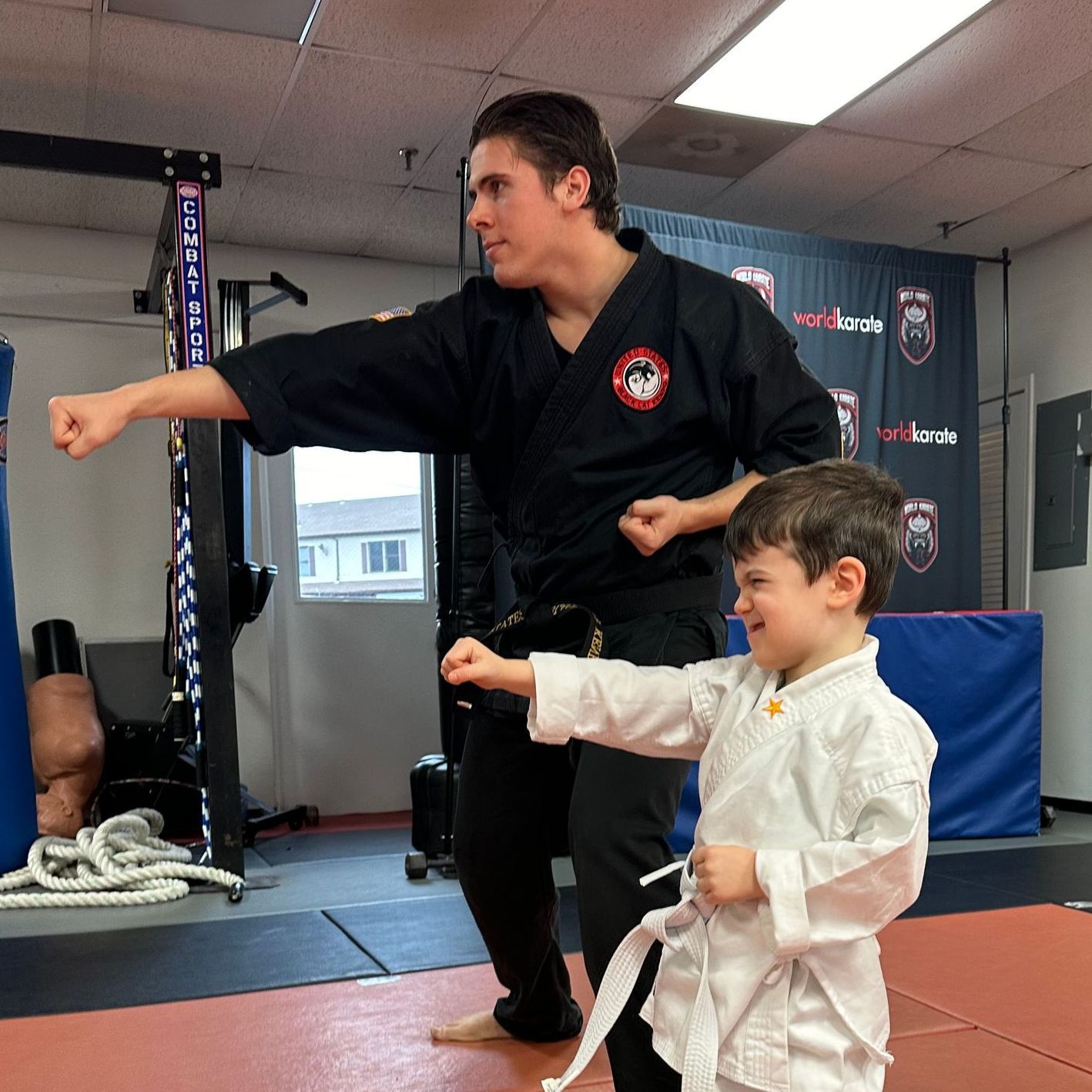 A man is kneeling down next to a young boy in a taekwondo class.