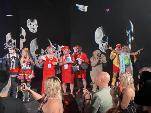 A group of costumed people on a stage. Some are tossing money into the air while a crowd applauds.