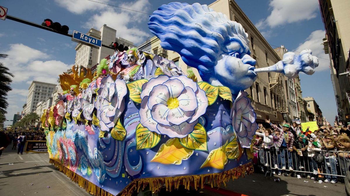 Mardi Gras float with a blue face blowing a cloud. People line the street.