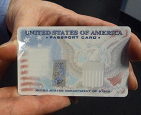 A hand holding a United States passport card with eagle and flag designs.