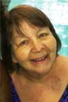 Smiling older woman, tan skin, dark hair, in a blue swimsuit near a pool.