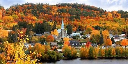 A colorful autumn scene of a small town nestled at the base of a hill covered in vibrant trees.